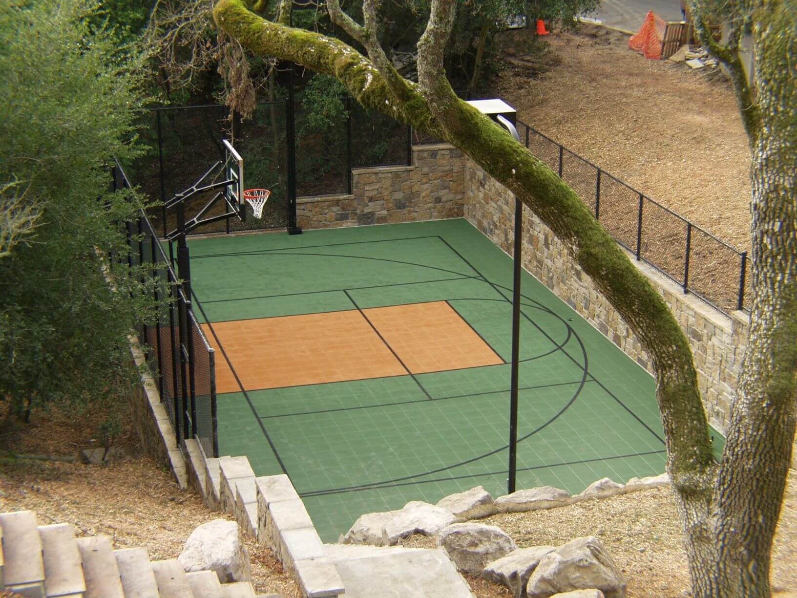 Residential backyard basketball half-court with blue and gray acrylic coating, single hoop, surrounded by lawn