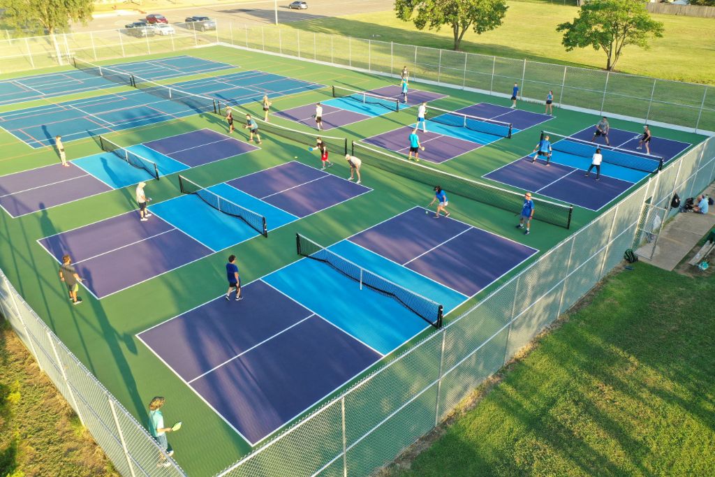 Aerial view of active multi-court pickleball facility with players on blue, purple and green SportMaster acrylic courts