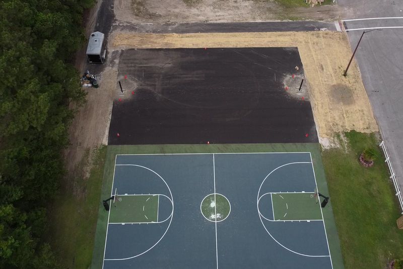 Before: fresh asphalt pad beside the existing court, aerial view