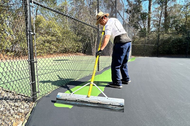 Close view of the squeegee pulling green acrylic across the court