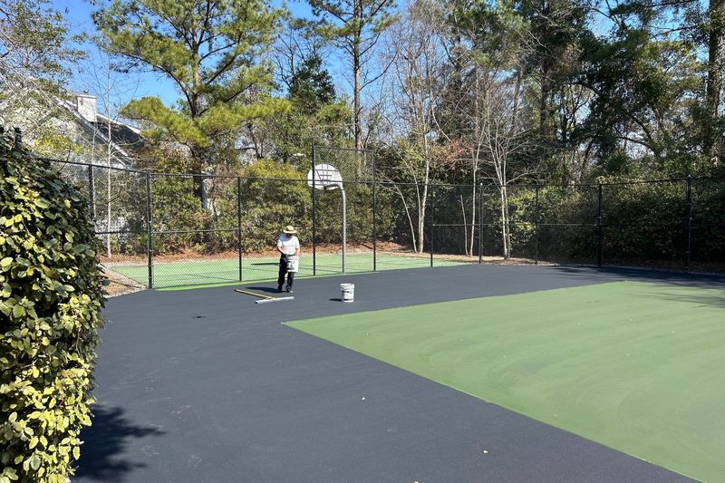 Crew member coating the court edge along the fence
