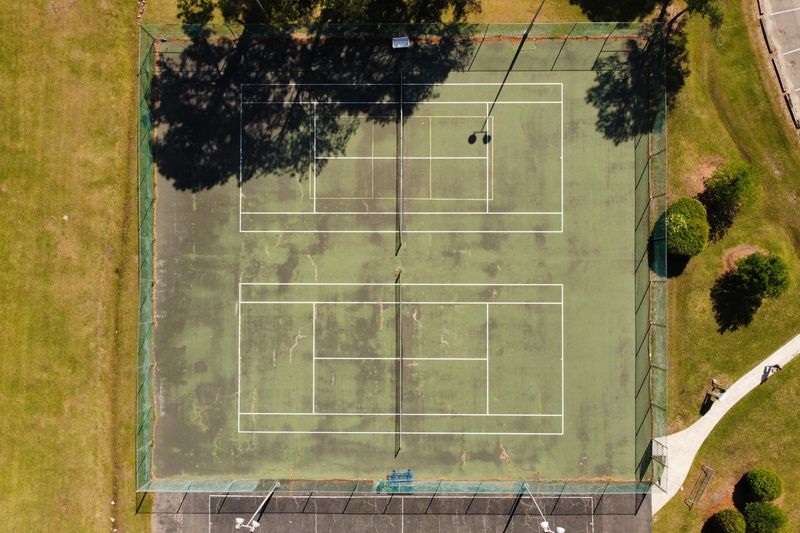Before: faded and worn tennis court surface, aerial view