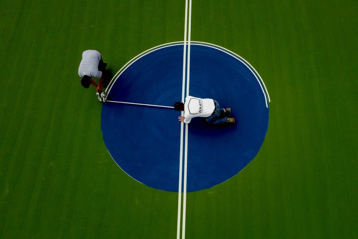 Overhead: crew painting the center circle and lines on a blue and green basketball court — East Arcadia, NC
