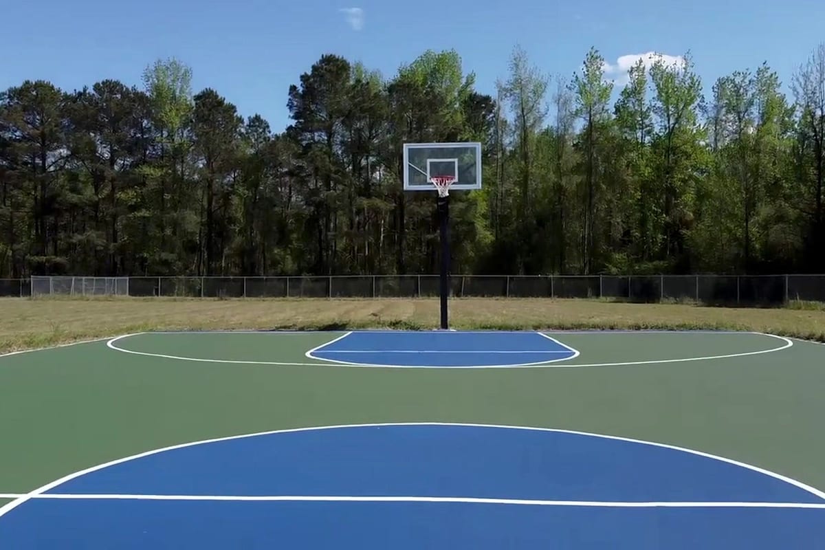 Finished blue and green outdoor basketball court with white lines and new goal, pines behind — East Arcadia, NC