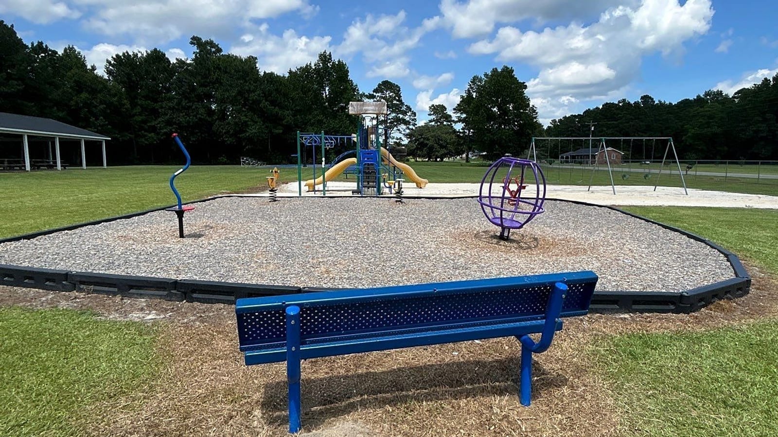 New blue park bench on a concrete pad with a playground and swings behind — Sandyfield, NC