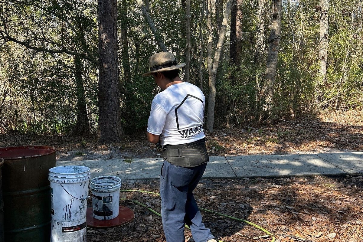 Crew member mixing acrylic sport-court coating in drums beside the court — Wilmington, NC