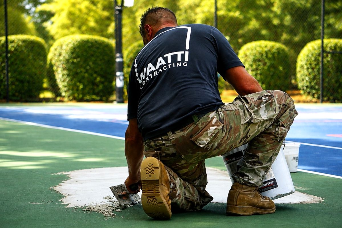 Waatti crew member kneeling on a court surface, troweling acrylic patch compound into a repaired area before recoating