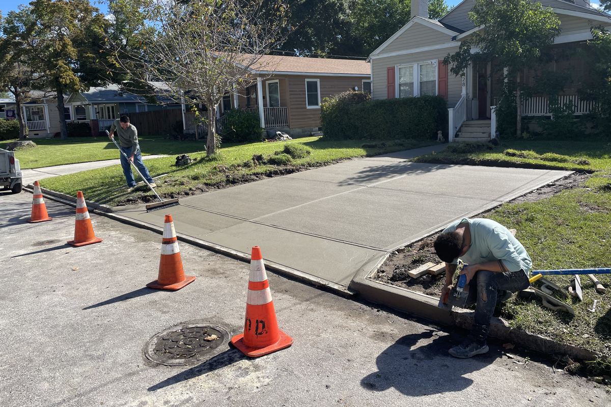 Waatti crew finishing a freshly poured concrete driveway apron and curb with traffic cones in place